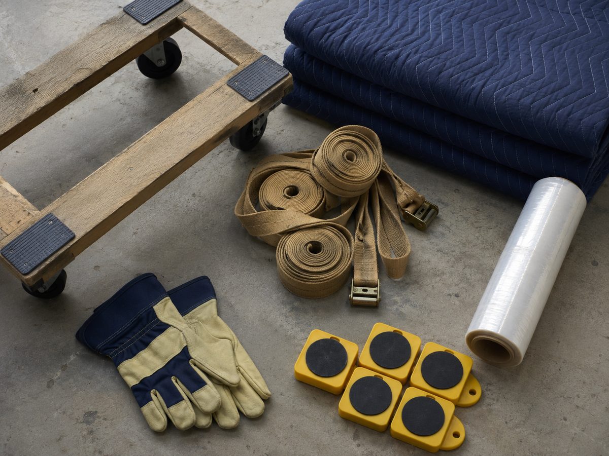 Moving equipment laid out: furniture dolly, straps, quilted blankets, stretch wrap, sliders and work gloves.